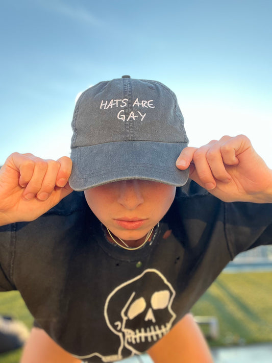 individual wearing a charcoal dad hat with the embroidered catchphrase "hats are gay" to celebrate queer pride