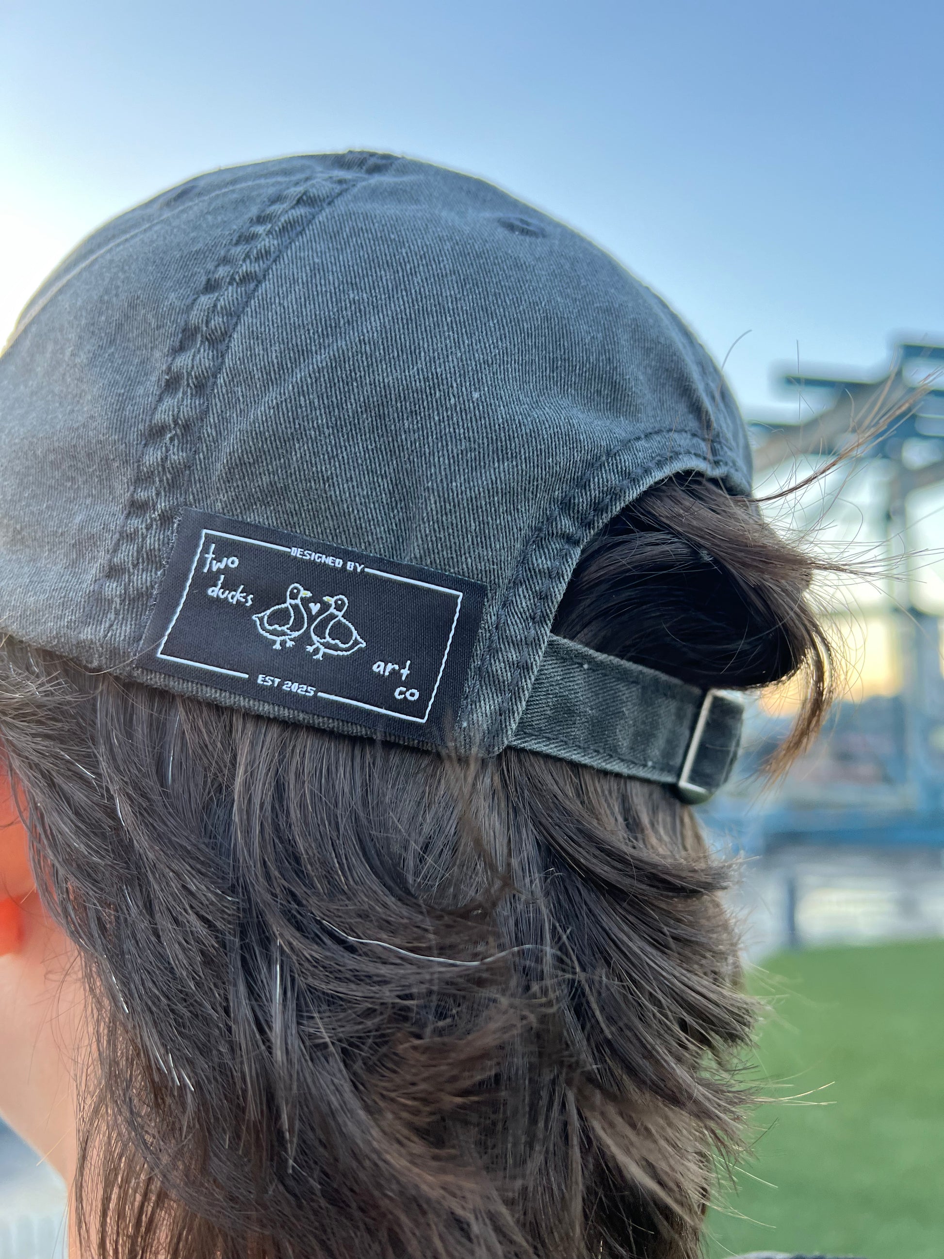 side of an individual's head wearing a charcoal dad hat with the logo tag visible stating "two ducks art co"